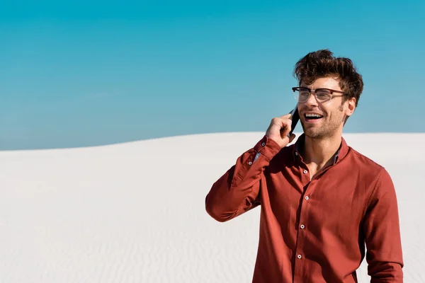 Щасливий чоловік на піщаному пляжі говорить на смартфоні проти чистого блакитного неба — стокове фото