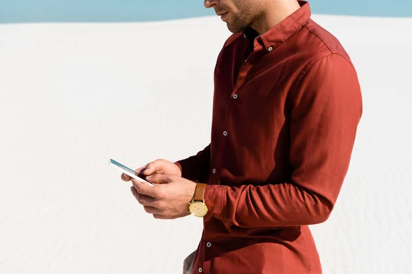 Ausgeschnittene Ansicht eines Mannes am Sandstrand per Smartphone — Stockfoto