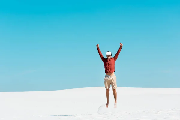 Hombre en la playa de arena en vr auriculares saltando contra el cielo azul claro - foto de stock