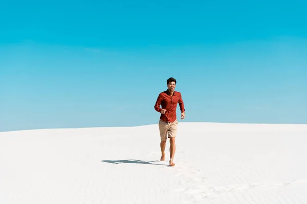 Hombre feliz corriendo en la playa de arena contra el cielo azul claro - foto de stock