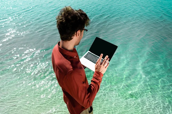 Handsome freelancer with laptop standing in turquoise water — Stock Photo