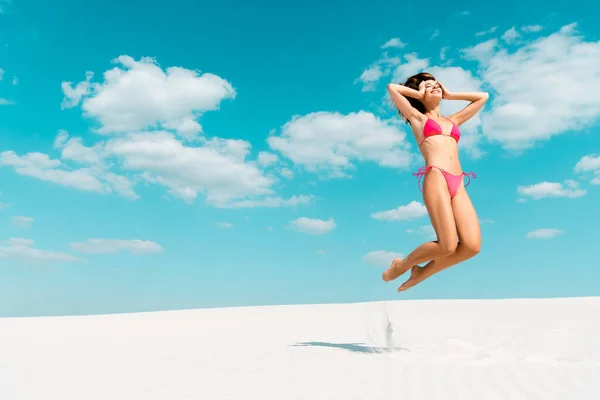 Feliz hermosa chica sexy en traje de baño saltando en la playa de arena con cielo azul y nubes - foto de stock