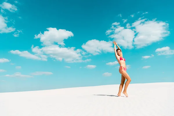 Sorrindo bela menina sexy em maiô com as mãos no ar na praia de areia com céu azul e nuvens — Fotografia de Stock