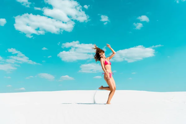 Sonriente hermosa chica sexy en traje de baño saltando en la playa de arena con cielo azul y nubes — Stock Photo
