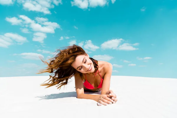 Sonriente hermosa chica sexy en traje de baño acostado en la playa de arena con el cielo azul y las nubes en el fondo - foto de stock