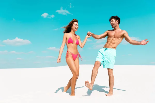 Feliz joven pareja cogida de la mano en la playa de arena - foto de stock