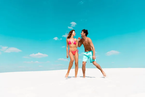 Sorridente giovane coppia che si tiene per mano sulla spiaggia di sabbia — Foto stock