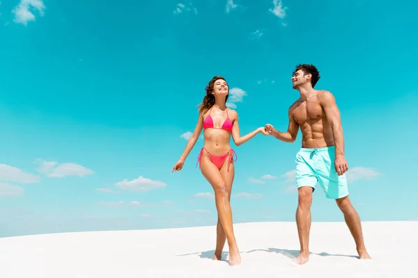 Smiling young couple holding hands on sandy beach — Stock Photo