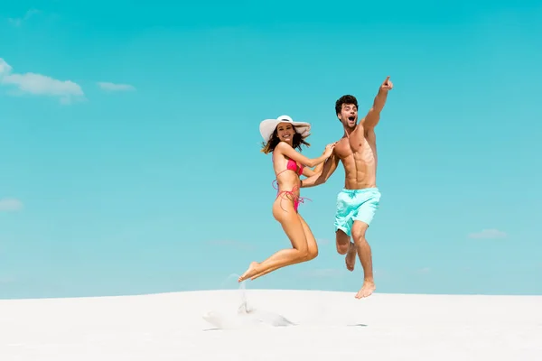 Sonriente joven pareja saltando juntos en la playa de arena - foto de stock