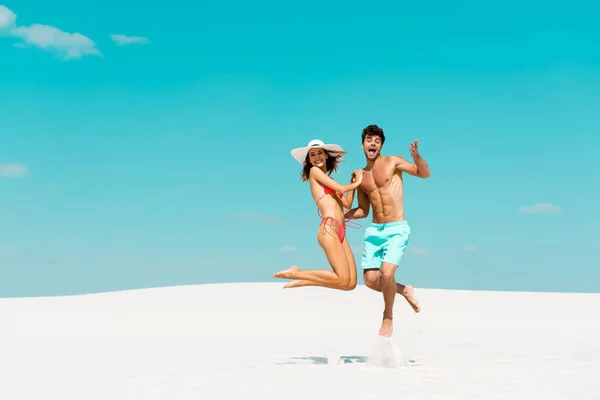 Sourire jeune couple sautant ensemble sur la plage de sable — Photo de stock