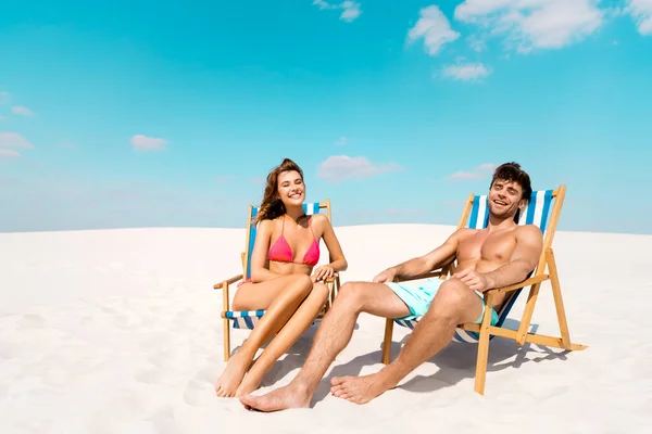 Sorridente giovane coppia seduta su sedie a sdraio sulla spiaggia di sabbia — Foto stock