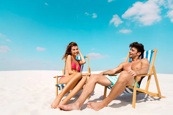 Sorridente giovane coppia seduta su sedie a sdraio sulla spiaggia di sabbia — Foto stock