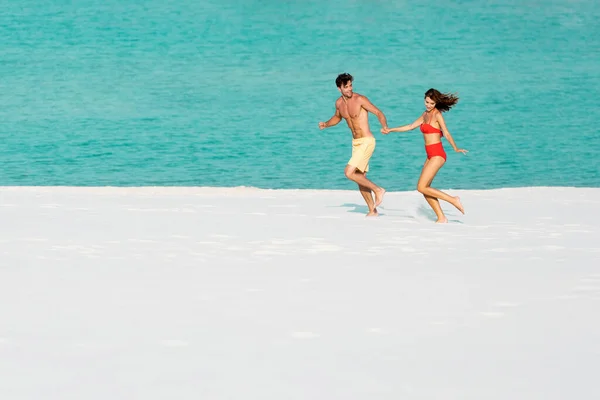 Joven sexy pareja corriendo en arena playa cerca de océano - foto de stock