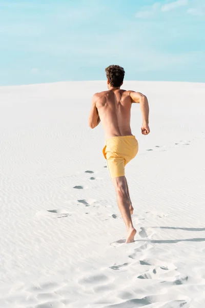 Вид сзади человека в купальниках с мускулистым торсом, бегущего по песчаному пляжу — стоковое фото