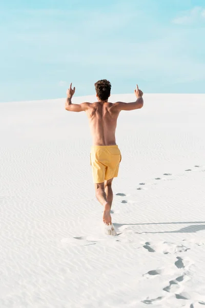 Vista trasera del hombre en pantalones cortos de natación con torso muscular corriendo en la playa de arena — Stock Photo