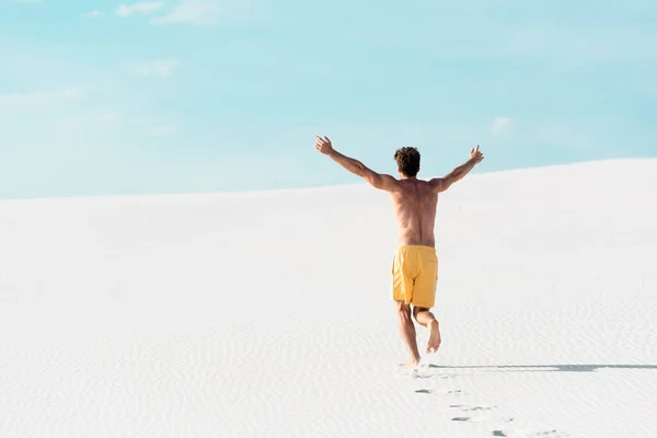 Visão traseira do homem em calções de natação com tronco muscular correndo na praia arenosa — Fotografia de Stock