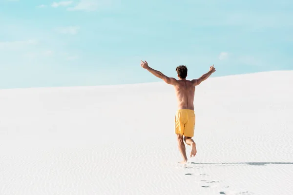 Vista trasera del hombre en pantalones cortos de natación con torso muscular corriendo en la playa de arena — Stock Photo