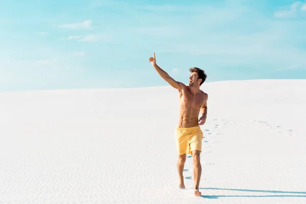 Hombre en pantalones cortos de natación con torso muscular caminando en la playa de arena - foto de stock