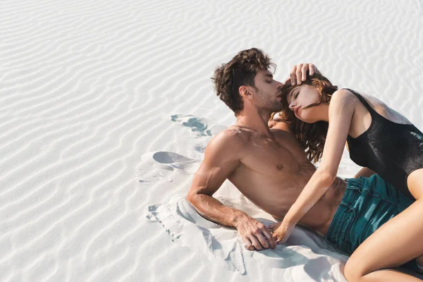 Sexy young man kissing girlfriend on sandy beach — Stock Photo