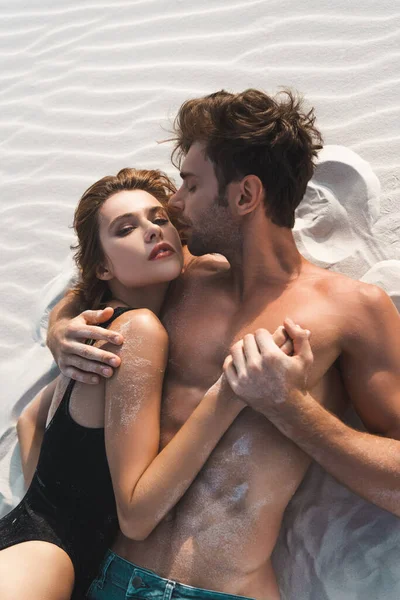 Vista superior del joven sexy acostado y besándose con su novia en la playa de arena - foto de stock