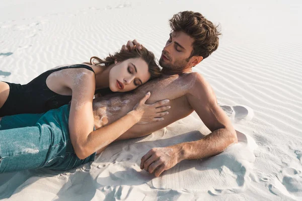 Sexy young man lying with girlfriend on sandy beach — Stock Photo