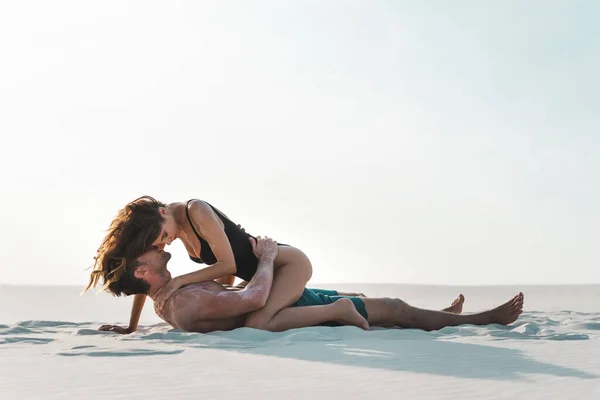 Vue latérale de sexy passionné jeune couple couché sur la plage de sable fin — Photo de stock