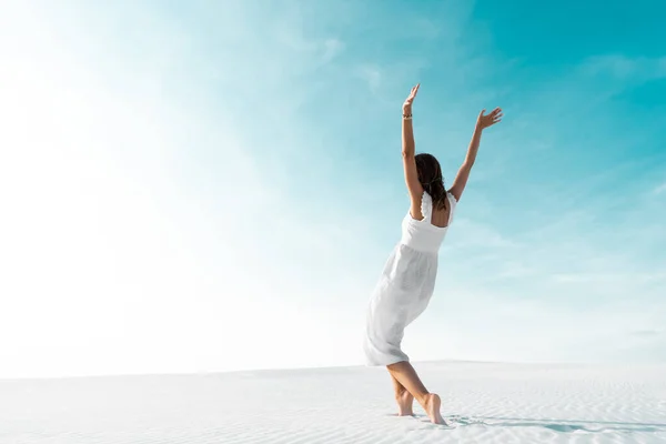 Hermosa chica en vestido blanco con las manos en el aire en la playa de arena con cielo azul - foto de stock