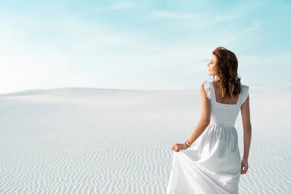 Vista trasera de la hermosa chica en vestido blanco en la playa de arena con cielo azul - foto de stock