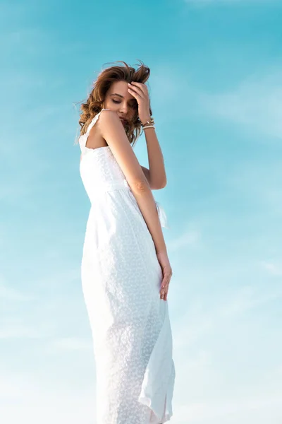 Низький кут зору красивої дівчини в білій сукні на блакитному небі — стокове фото