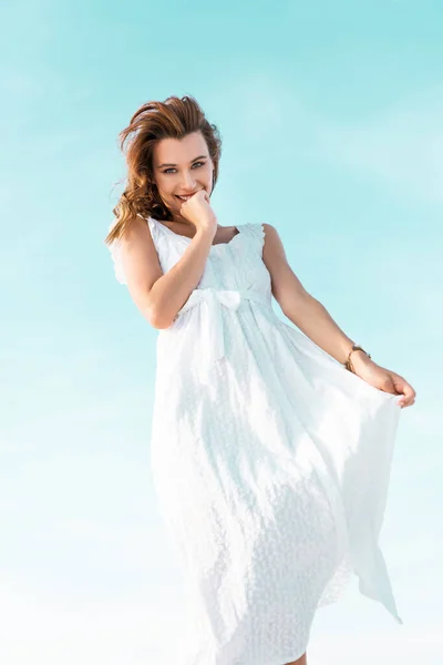 Low angle view of smiling beautiful girl in white dress against blue sky — Stock Photo