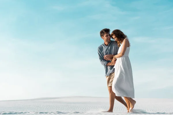 Sourire jeune couple marchant sur la plage de sable contre le ciel bleu — Photo de stock