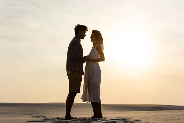 Вид збоку молода пара тримає руки на піщаному пляжі на заході сонця — стокове фото
