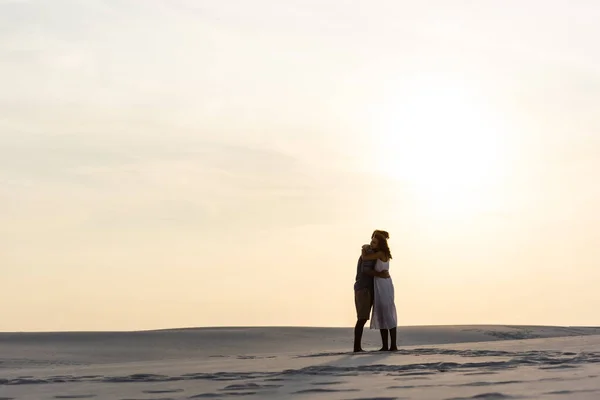 Vista lateral do jovem casal abraçando na praia de areia ao pôr do sol — Fotografia de Stock