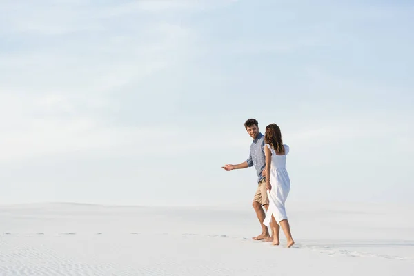 Jovem casal andando na praia de areia contra o céu azul — Fotografia de Stock