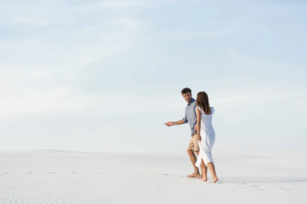 Pareja joven caminando en la playa de arena contra el cielo azul - foto de stock