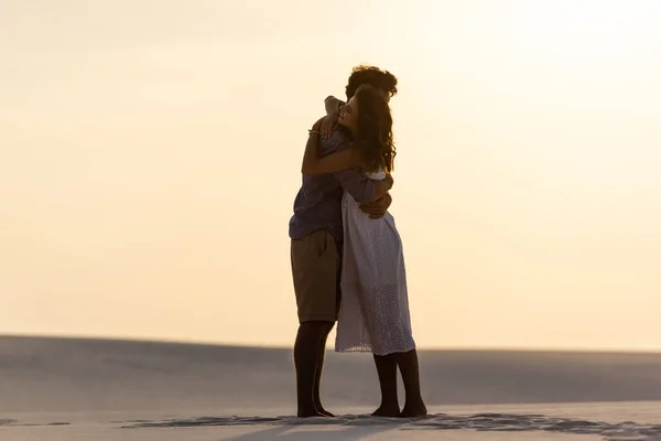 Vue latérale de jeune couple étreignant sur la plage de sable au coucher du soleil — Photo de stock