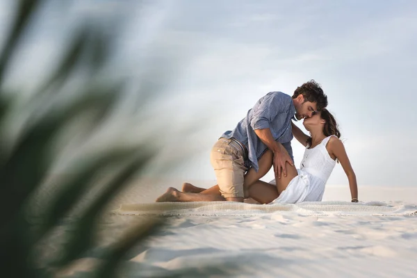 Избирательный фокус страстной молодой пары, целующейся на одеяле на пляже — стоковое фото