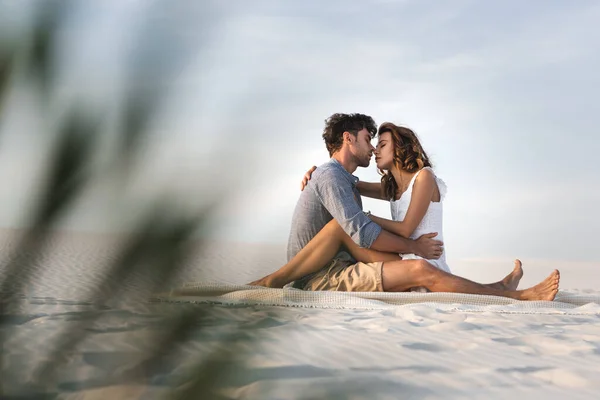 Selektiver Fokus leidenschaftlicher junger Paare, die sich auf einer Decke am Strand küssen — Stockfoto