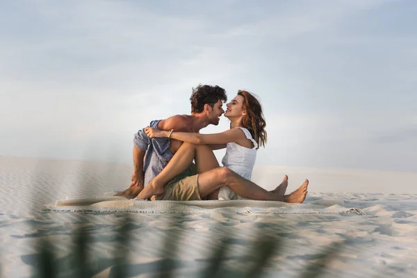Избирательный фокус страстной молодой пары, целующейся на одеяле на пляже — стоковое фото