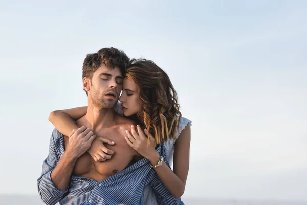 Leidenschaftliche junge Frau berührt Freund-Oberkörper vor blauem Himmel — Stockfoto