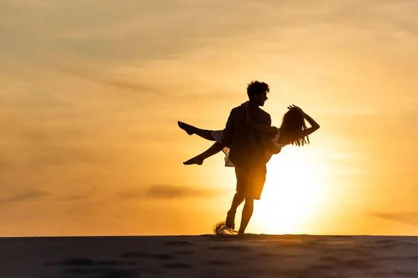 Silhouettes of man and woman dancing on beach against sun during sunset — Stock Photo