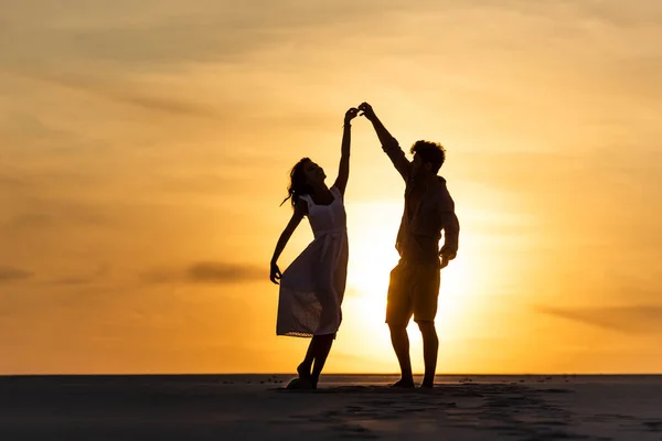 Silhuetas de homem e mulher dançando na praia contra o sol durante o pôr do sol — Fotografia de Stock