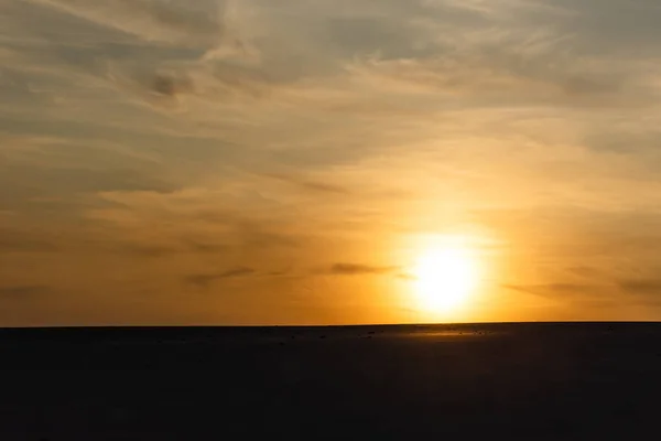 Praia de areia escura contra o sol brilhante durante o pôr do sol — Fotografia de Stock