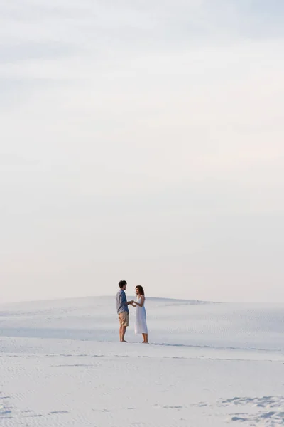 Пара стоїть на піщаному пляжі і тримає руки з блакитним небом — стокове фото