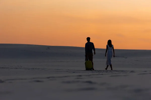 Back view of couple walking on beach with travel bag at sunset — Stock Photo