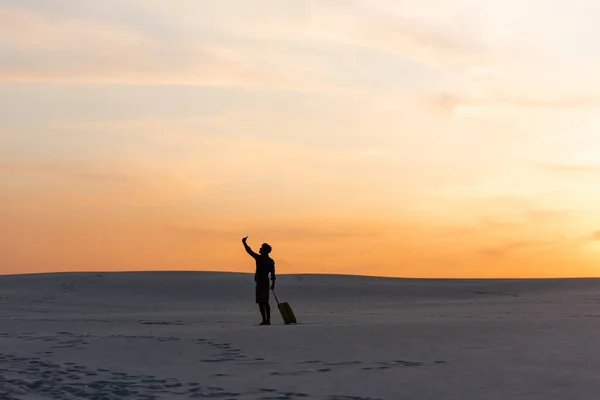 Silhouette dell'uomo che cammina sulla spiaggia con borsa da viaggio e smartphone al tramonto — Foto stock