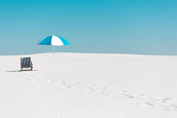 Cadeira deck e guarda-chuva na praia de areia com vestígios contra o céu azul claro — Fotografia de Stock