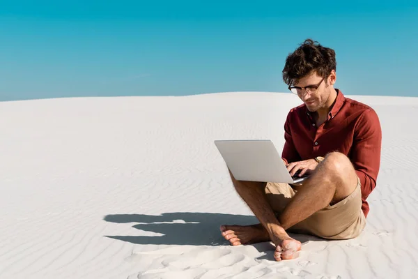 Jovem freelancer na praia de areia usando laptop contra céu azul claro — Fotografia de Stock