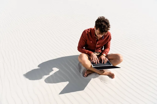 Joven freelancer sentado en la playa de arena con portátil - foto de stock