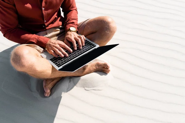 Обрізаний вид молодого фрілансера, що сидить на піщаному пляжі з ноутбуком — стокове фото